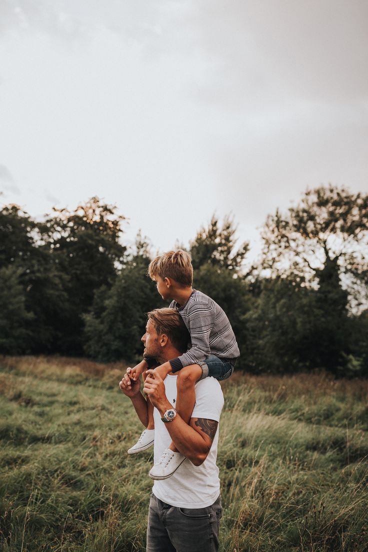 a man holding a young boy on his shoulders while standing in a field with tall grass