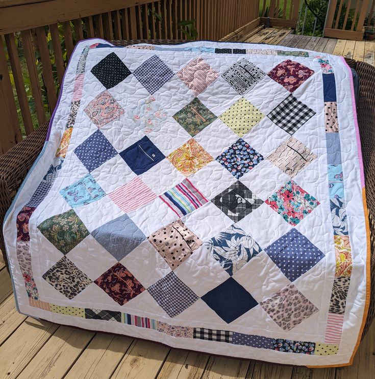 a quilted blanket sitting on top of a wooden deck next to a chair and table