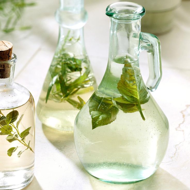 two glass bottles filled with water and green leaves next to each other on a table