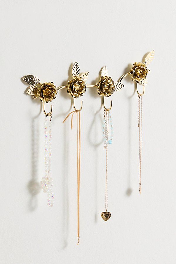 five different necklaces hanging from hooks on a white wall with beads and leaves attached to them