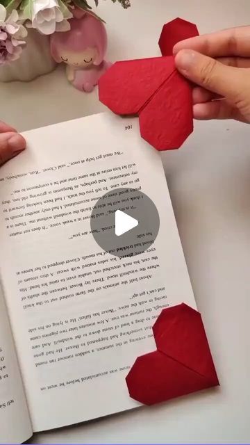 two hands holding origami hearts over an open book