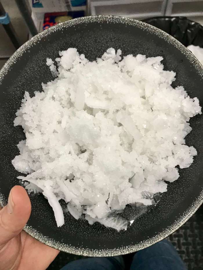 a black bowl filled with white sugar on top of a metal counter next to a person's hand