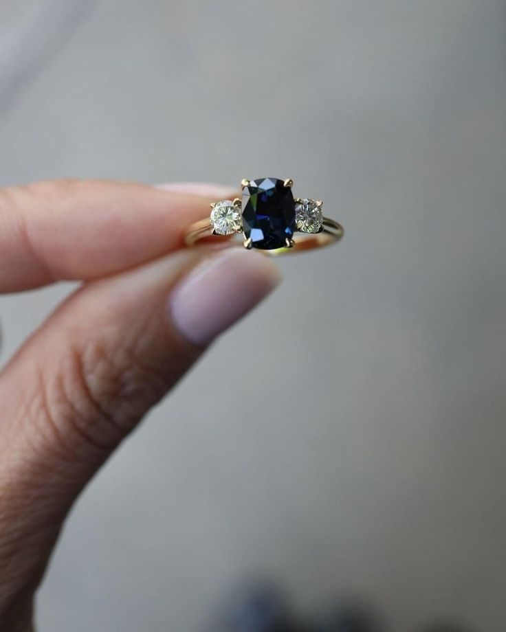 a woman's hand holding a ring with a blue stone and three diamonds on it