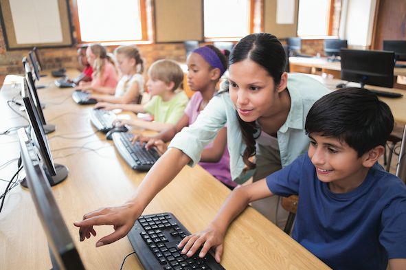 a group of children sitting in front of computer monitors with their hands on the keyboard