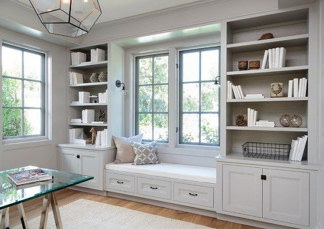 a window seat in front of two windows with bookshelves on either side and a glass top table