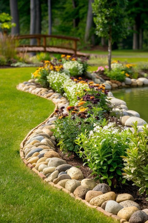 a garden with lots of rocks and flowers in the grass next to a pond that is surrounded by trees