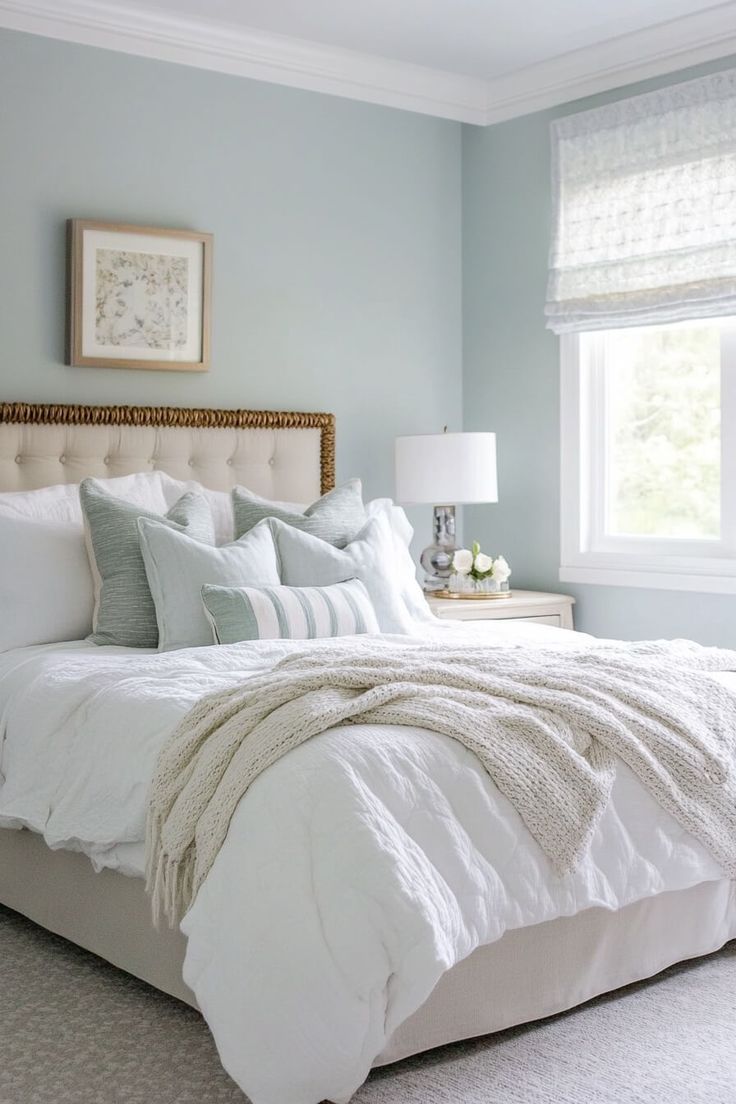 a white bed sitting under a window next to a nightstand with a lamp on it