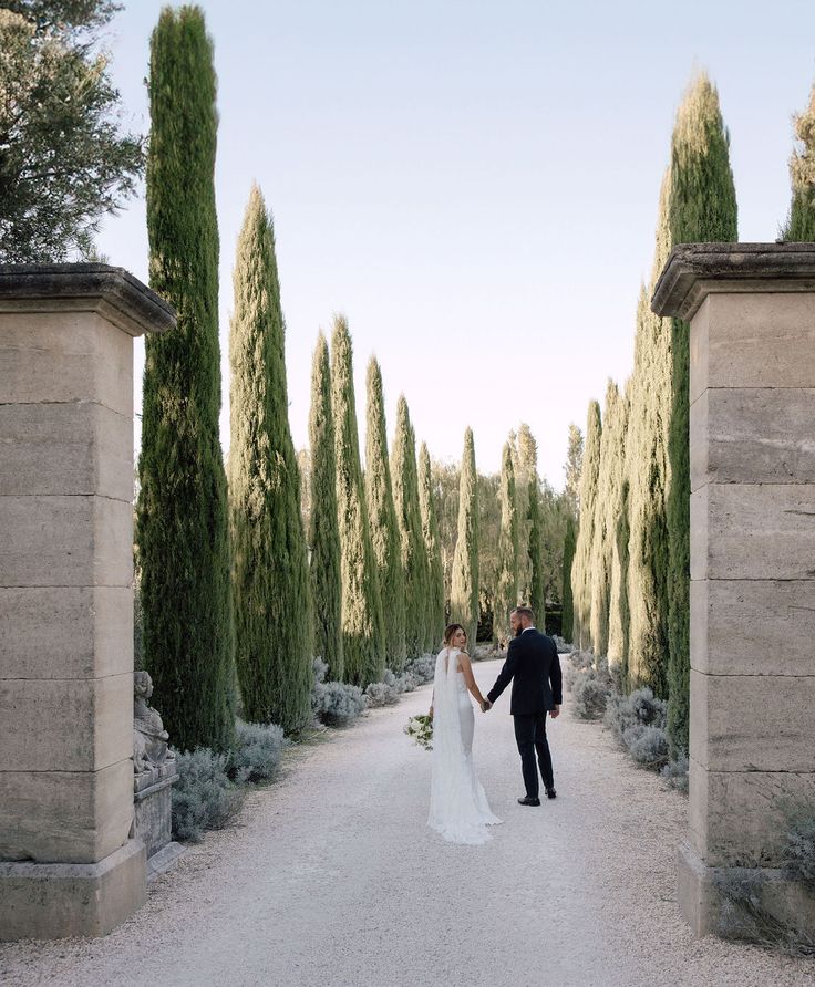 a bride and groom holding hands walking through an archway in the middle of a garden