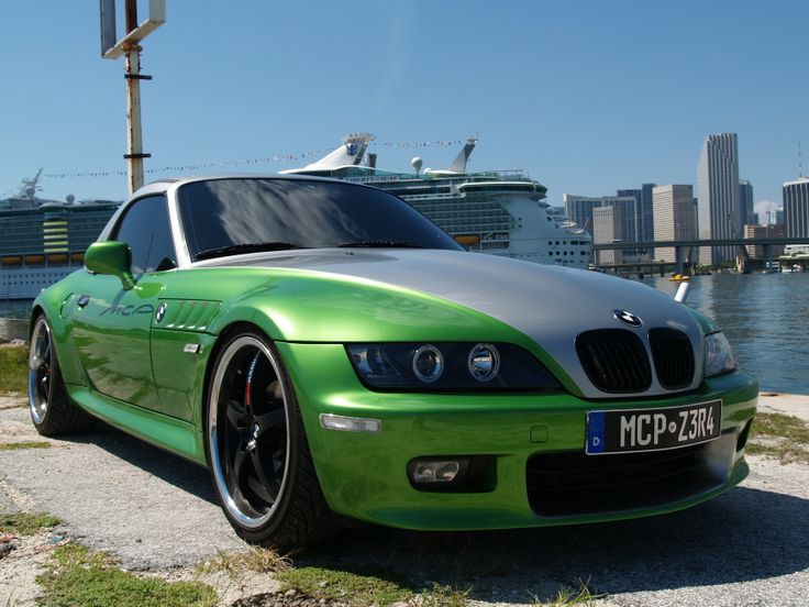 a green bmw car parked in front of a cruise ship on the water's edge