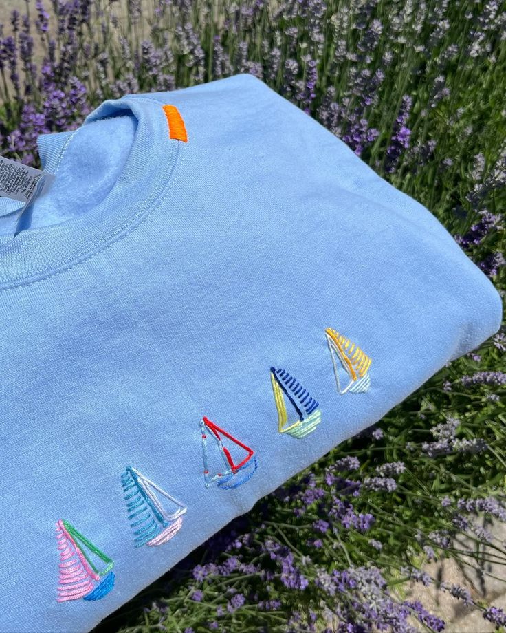 a blue shirt with sailboats embroidered on the front and back, sitting next to lavender flowers