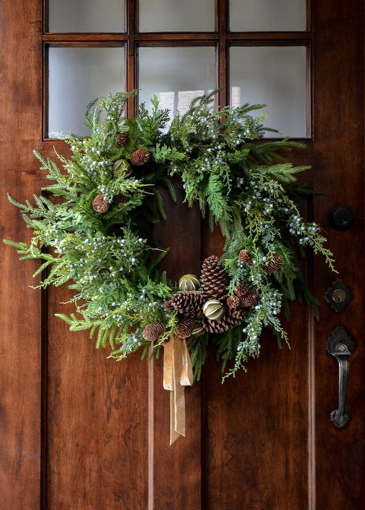 a wreath on the front door with pine cones and greenery hanging from it's side