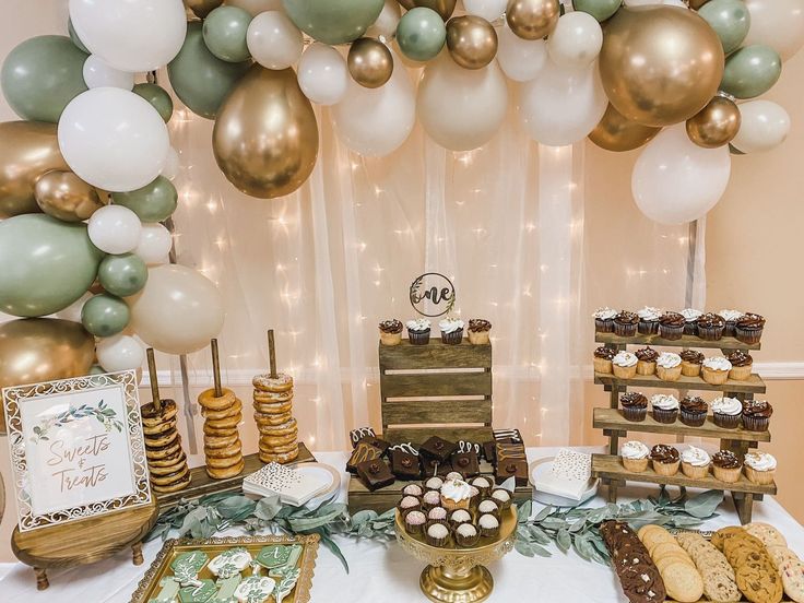 a dessert table with balloons, cookies and cupcakes