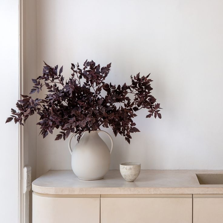 a white vase filled with purple flowers on top of a counter