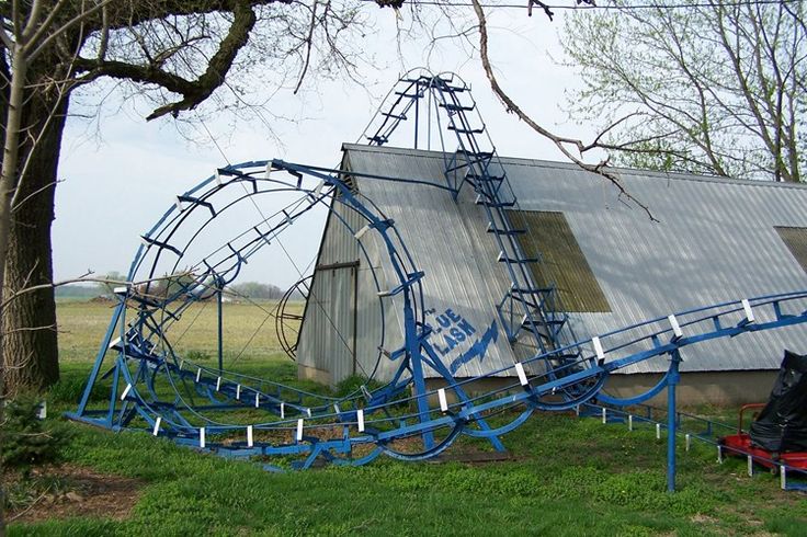 an abandoned roller coaster sits in the grass next to a building with a metal roof