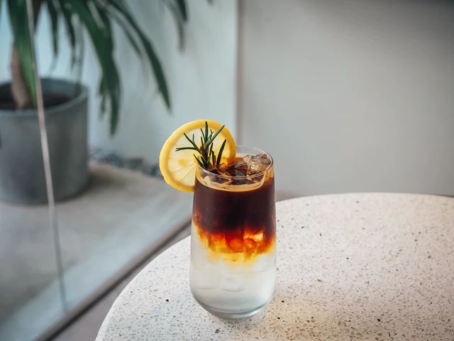 a close up of a drink on a table with a plant in the back ground