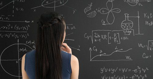 a woman standing in front of a blackboard with lots of calculations written on it