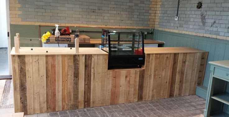 an unfinished kitchen with wooden counter tops and shelves on the wall, in front of a brick wall