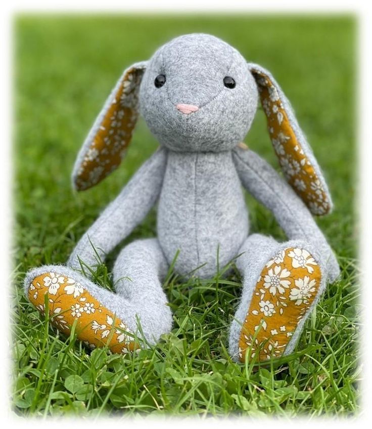 a gray stuffed animal sitting on top of a lush green grass covered field with white flowers