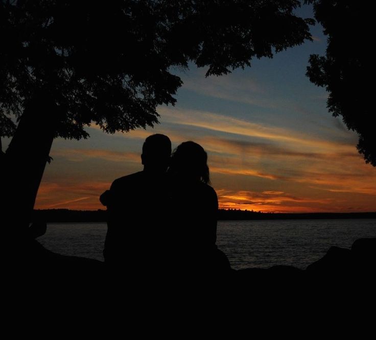 two people are silhouetted against an orange and blue sky at sunset by the water