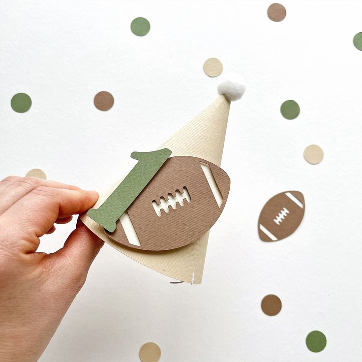 a hand holding a piece of paper with a football on it and a party hat