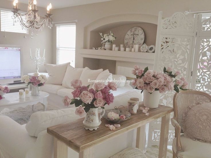 a living room with white furniture and pink flowers in vases on the coffee table