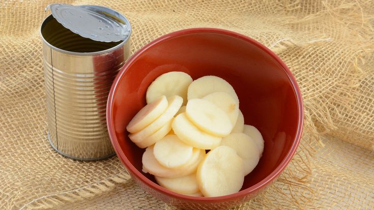 a red bowl filled with sliced up bananas next to a can of canned drink on a burlap cloth