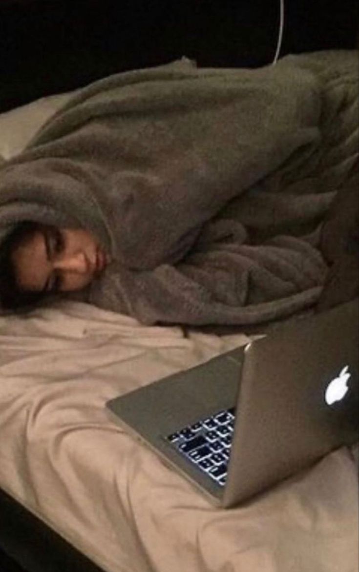 a woman laying in bed under a blanket next to an apple laptop