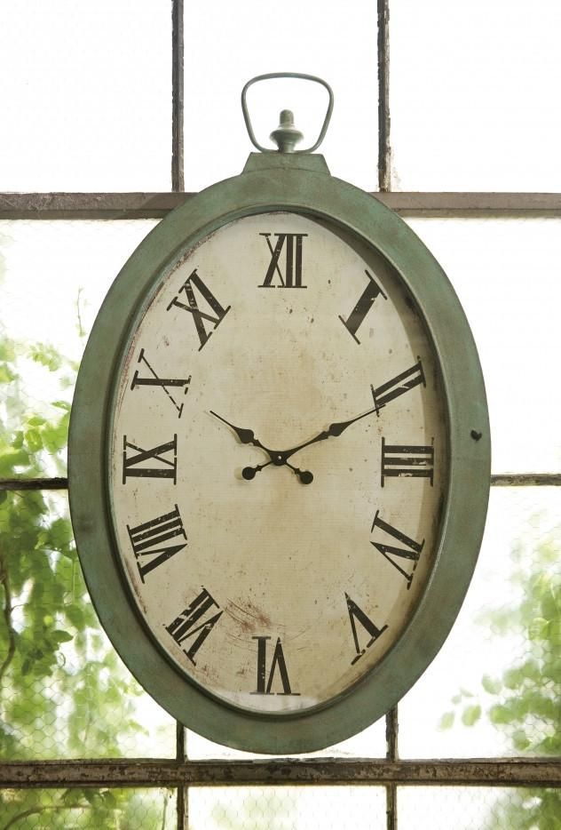 an old clock hanging from the side of a window sill in front of trees