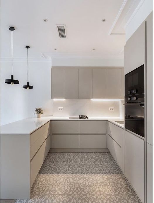 an empty kitchen with white counter tops and beige cabinets, along with black pendant lights