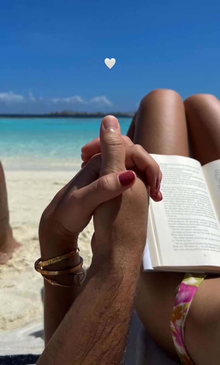 a person sitting on the beach reading a book with a white heart floating above them