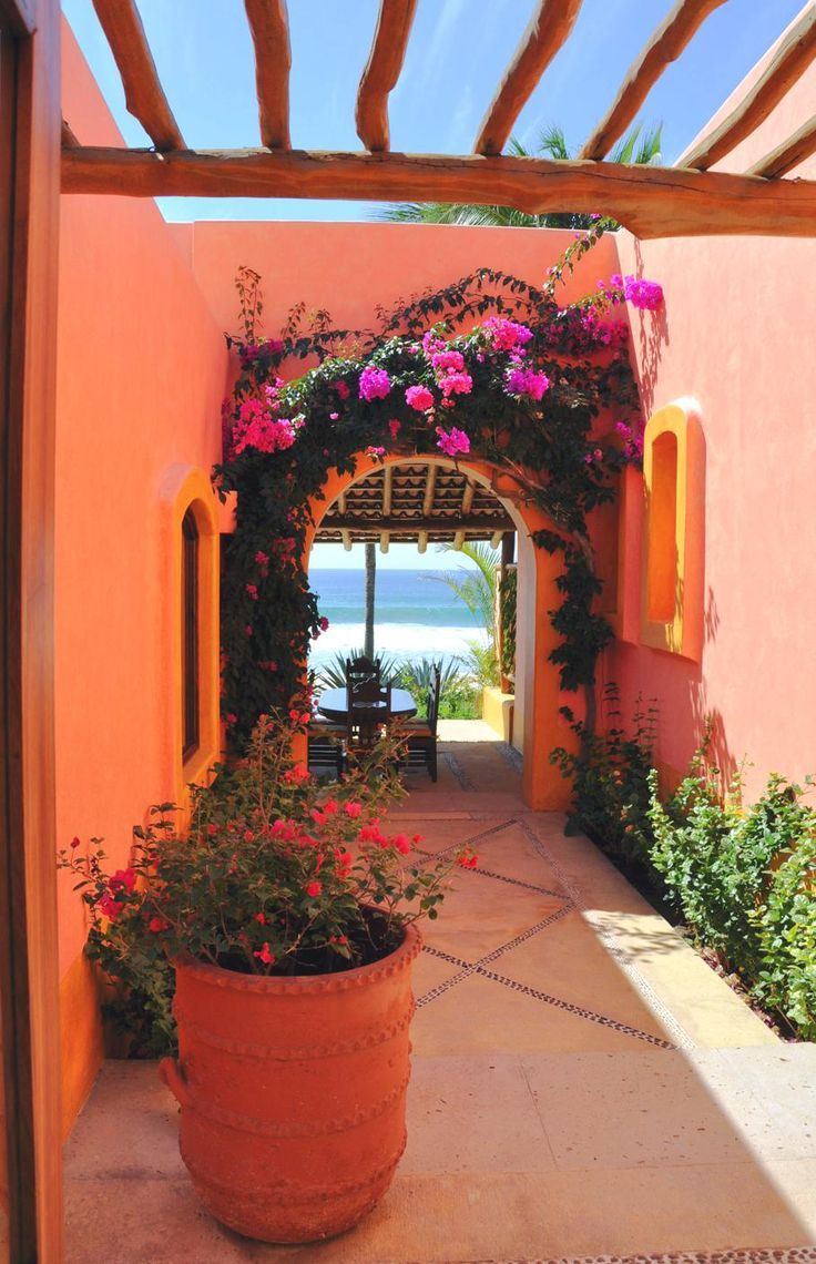 an orange building with pink flowers and greenery on the front door, along with a walkway