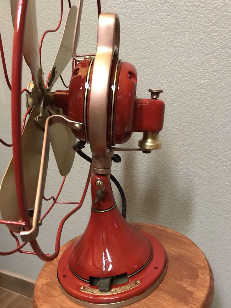 an old fashioned red fan sitting on top of a wooden table next to a wall