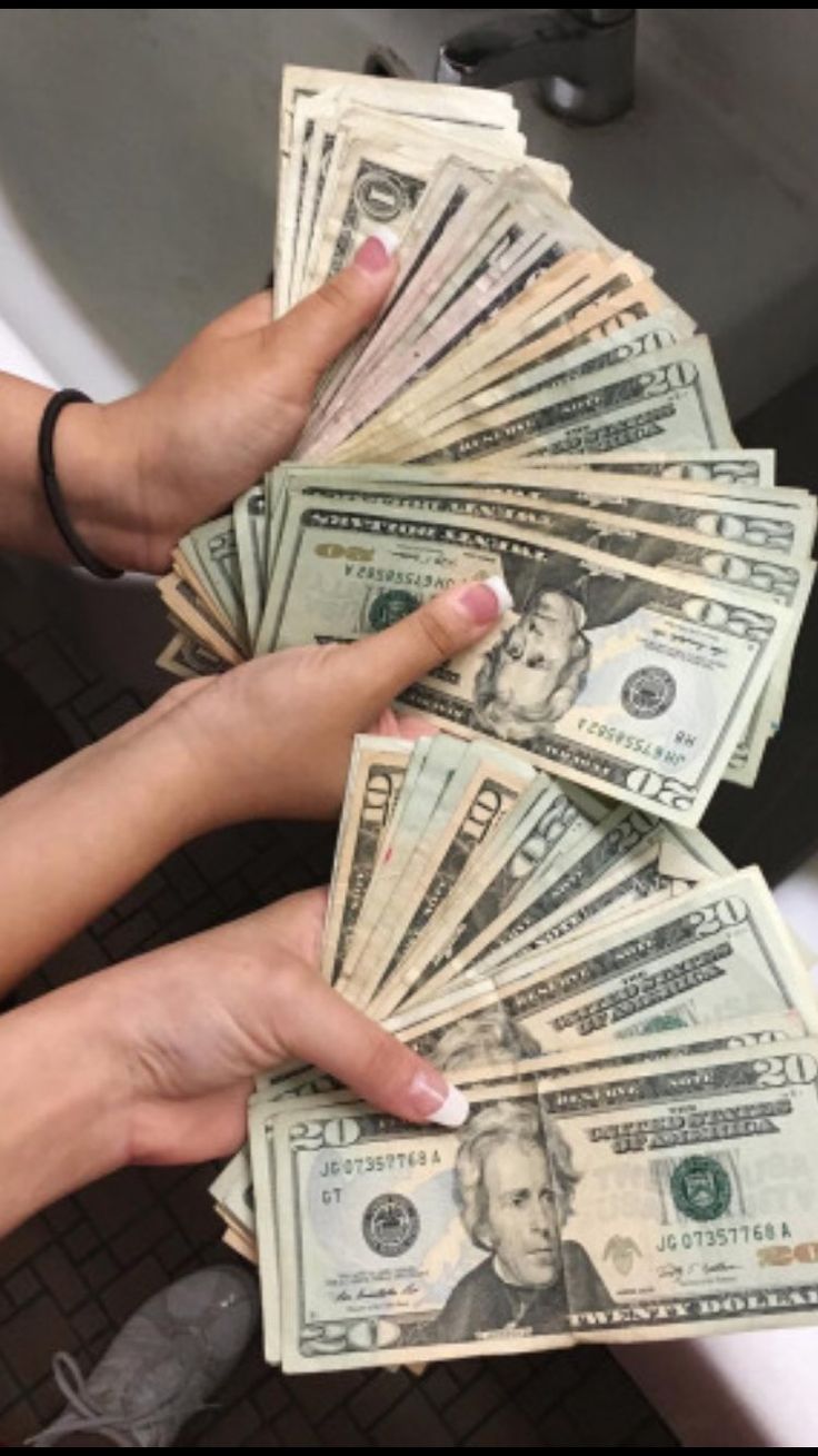 two hands holding stacks of one hundred dollar bills