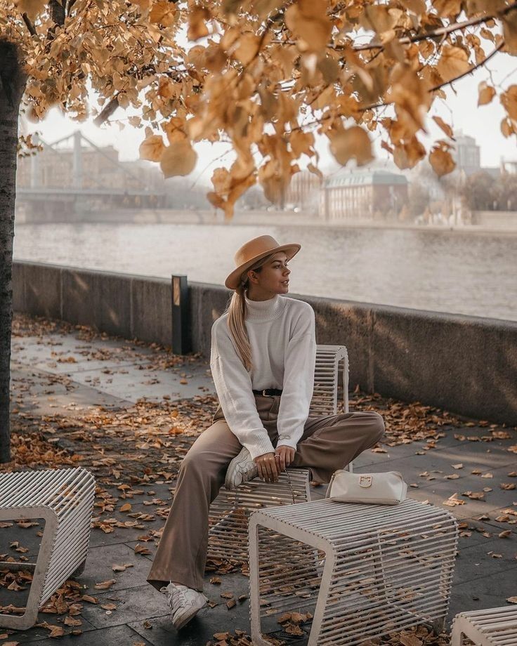 a woman sitting on top of a white chair next to a tree with leaves all over it