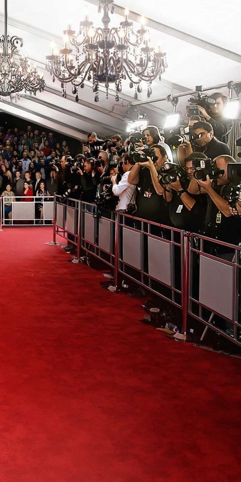 a woman is walking down the red carpet in front of people taking pictures with her cell phone