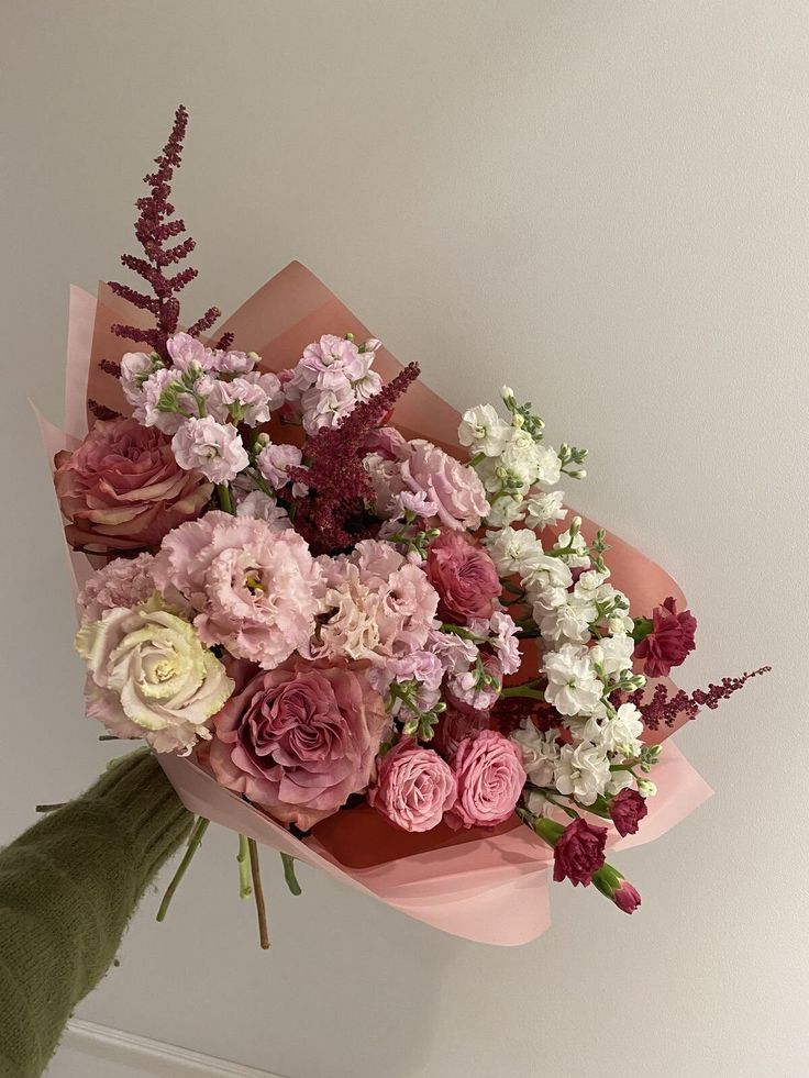 a bouquet of flowers sitting on top of a pink and white paper wrapper next to a wall