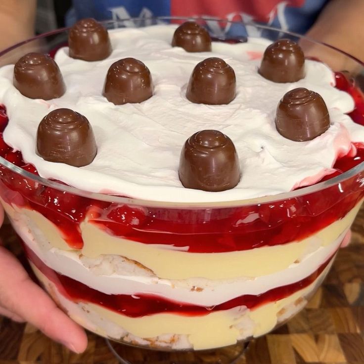 someone is holding up a dessert with chocolates on top and white frosting in the middle