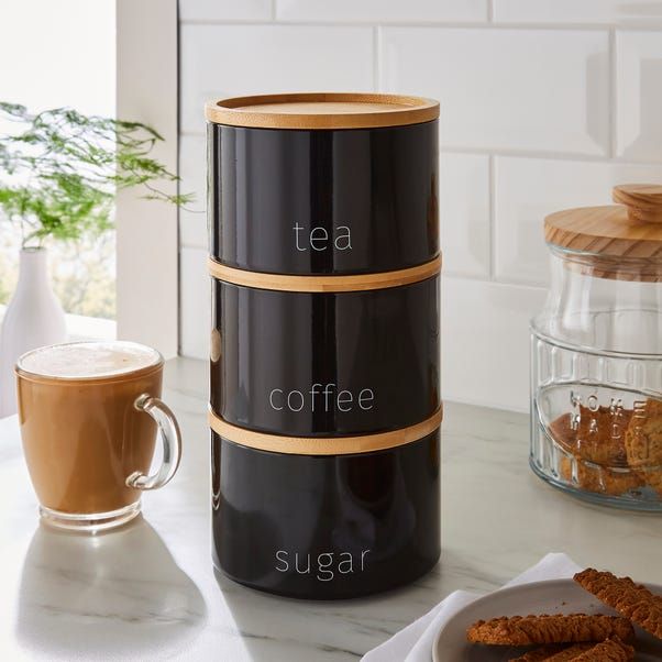 a stack of three black containers sitting on top of a counter next to a cup of coffee