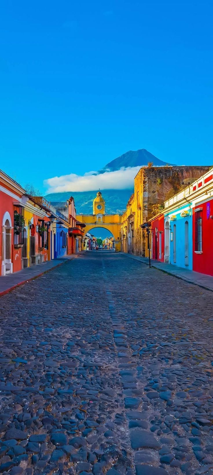 a cobblestone street lined with brightly colored buildings and mountains in the back ground