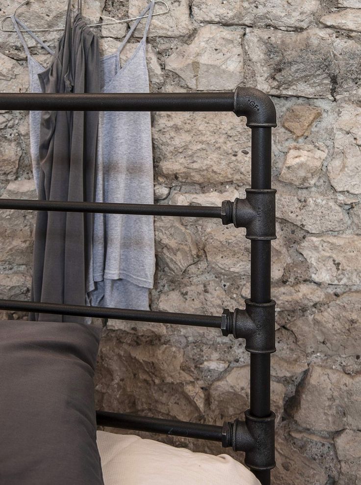 an iron bed frame with two pillows on it and some clothes hanging up against the wall