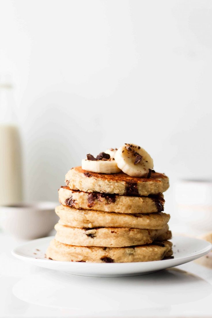 a stack of pancakes topped with bananas on a white plate next to a glass of milk