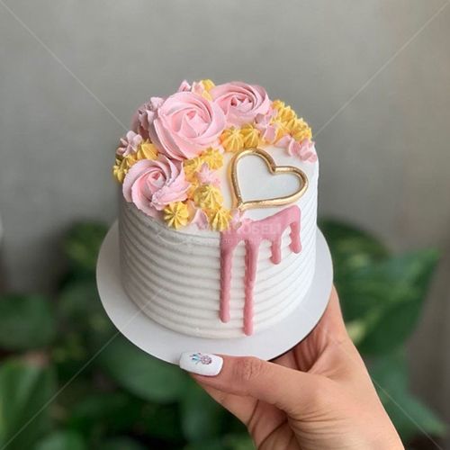 a hand holding a cake decorated with pink and yellow flowers on top of a white plate