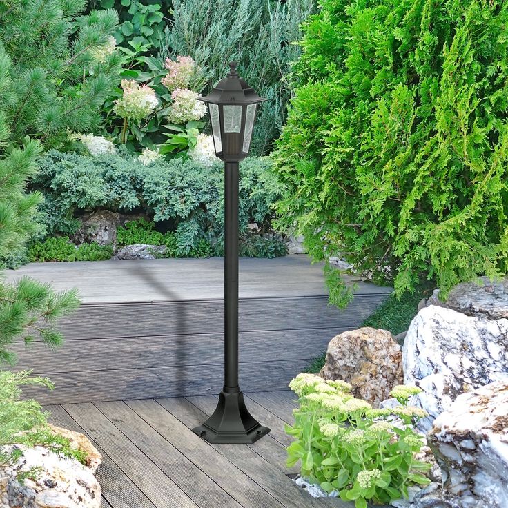 a lamp post in the middle of a wooden deck surrounded by plants and rocks,