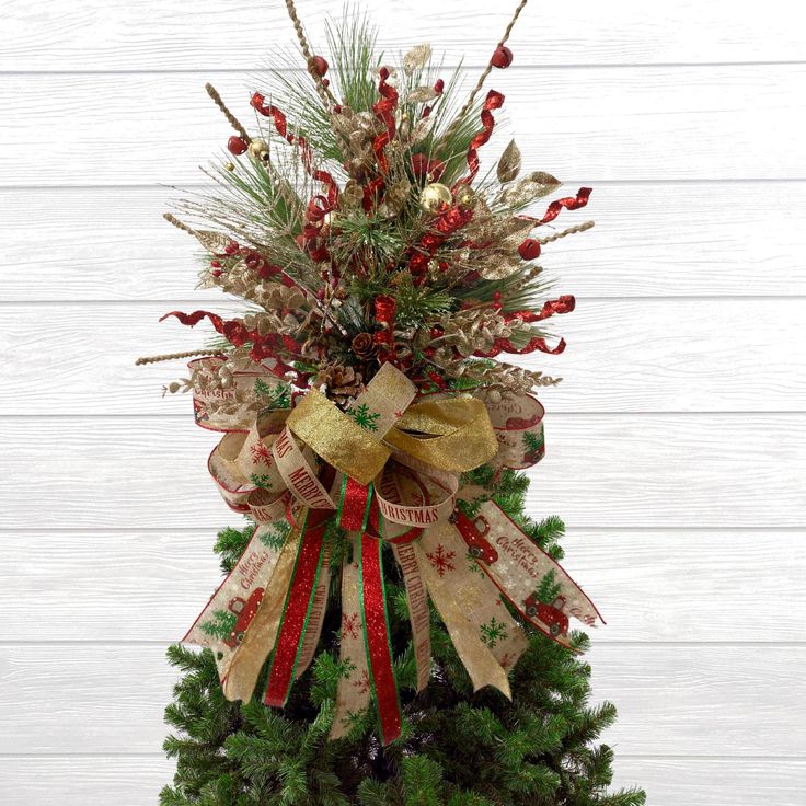 a christmas tree with red, white and gold ribbons on it's top is shown in front of a wooden wall