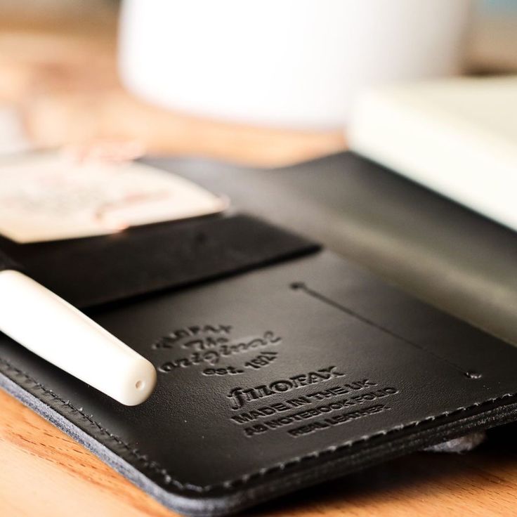 a wallet with a pen sticking out of it on top of a wooden table next to a keyboard