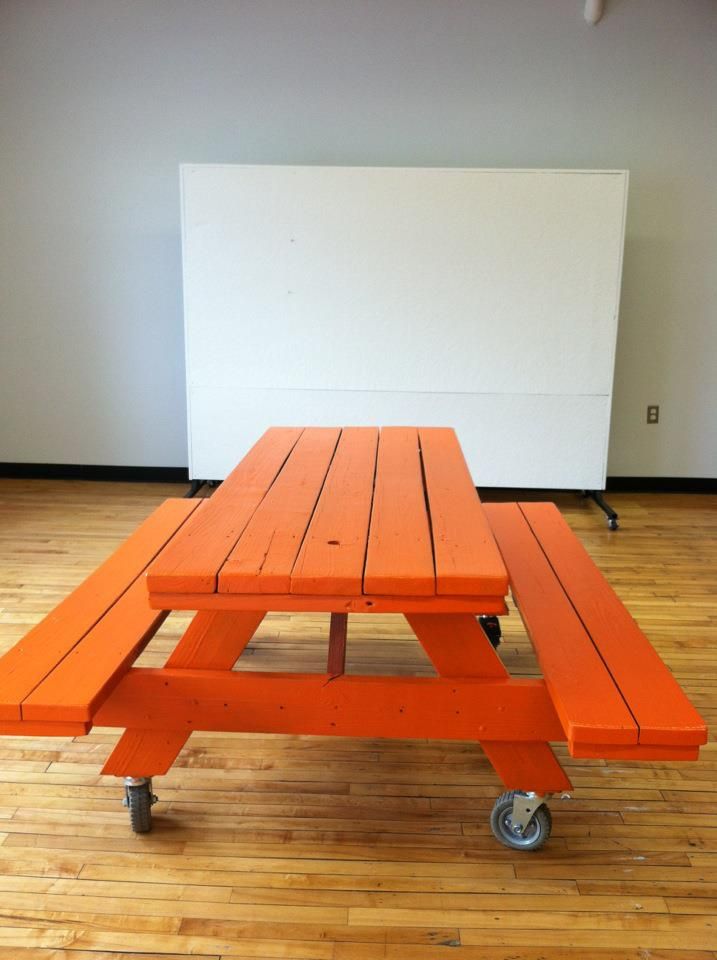 an orange picnic table sitting on top of a hard wood floor next to a white wall