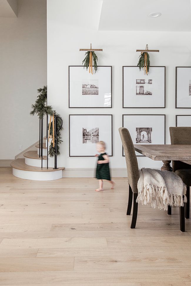 a child is walking in front of some pictures on the wall and a dining room table