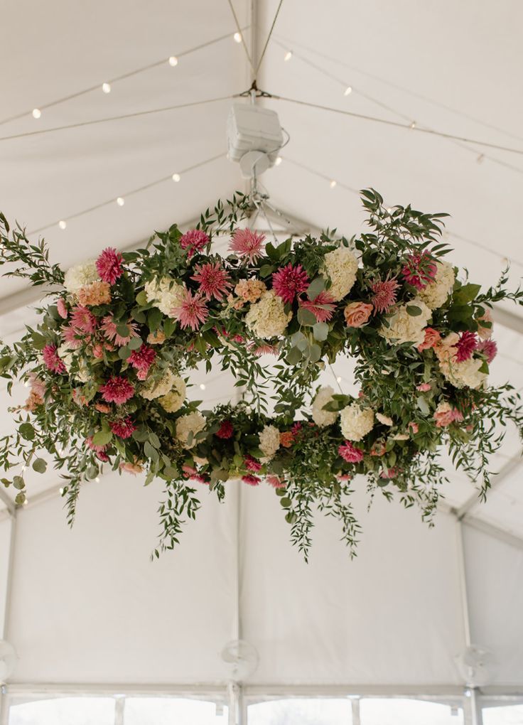 an overhead floral arrangement hangs from the ceiling in a marquee at a wedding