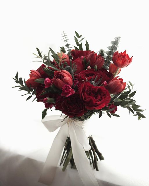 a bouquet of red flowers with greenery in the center on a white table cloth