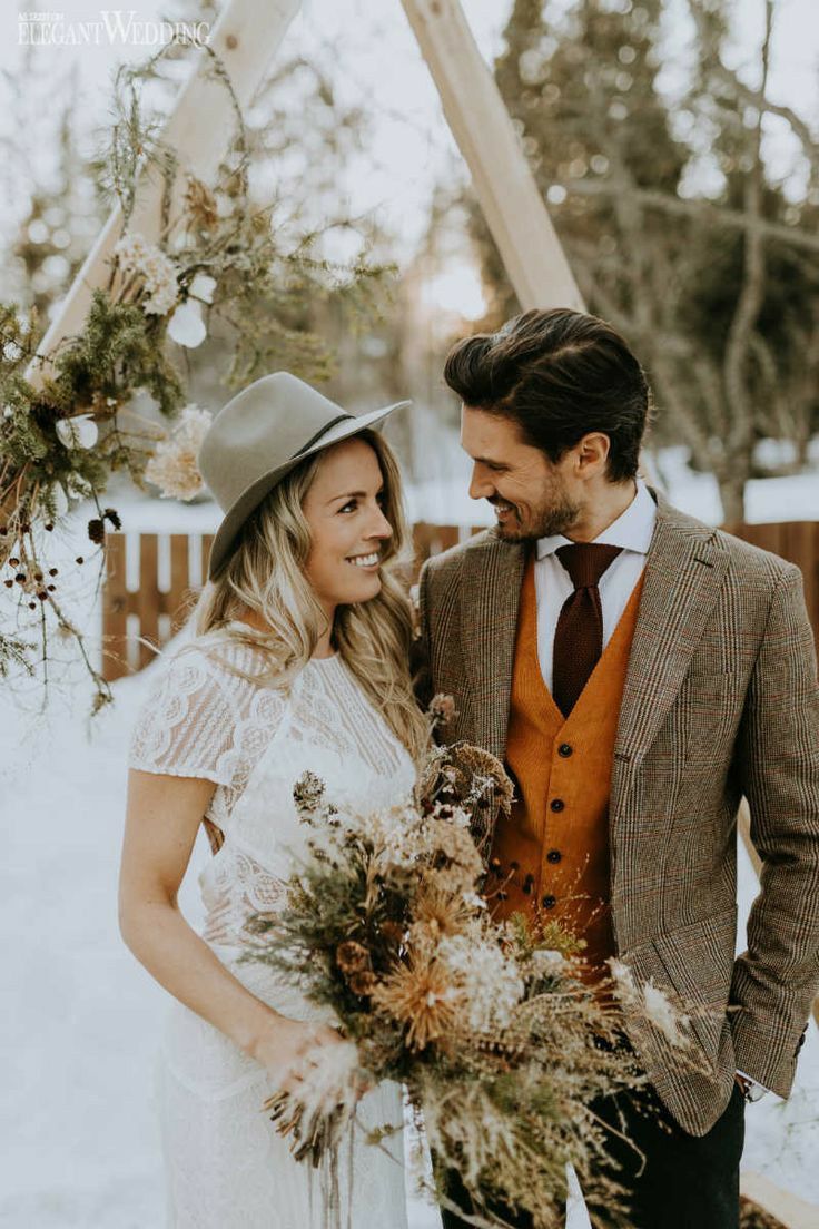 a man and woman standing next to each other in the snow with flowers on their bouquets